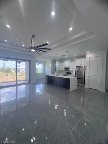Kitchen with refrigerator, a raised ceiling, dark marble finish floors, light countertops, and white cabinetry