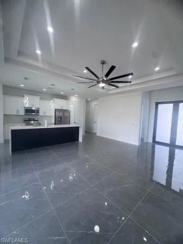 Unfurnished living room featuring a tray ceiling, ceiling fan, baseboards, and dark marble finish floors