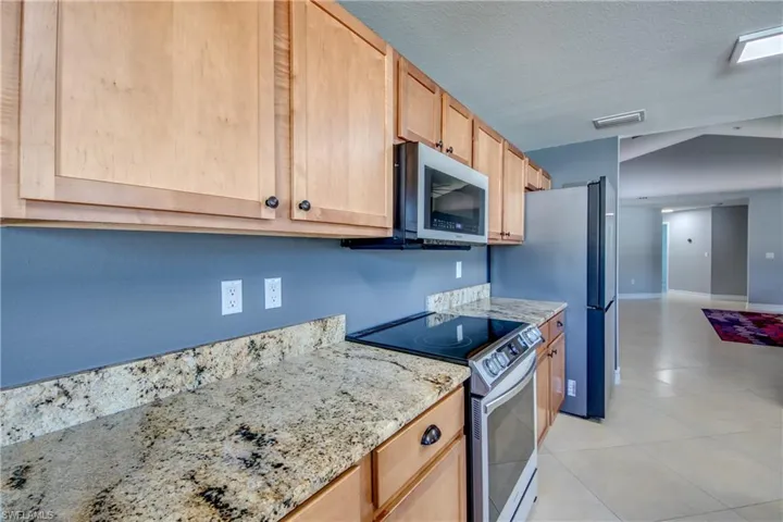 Kitchen with light brown cabinets, stainless steel appliances, light stone counters, a textured ceiling, and light tile patterned floors