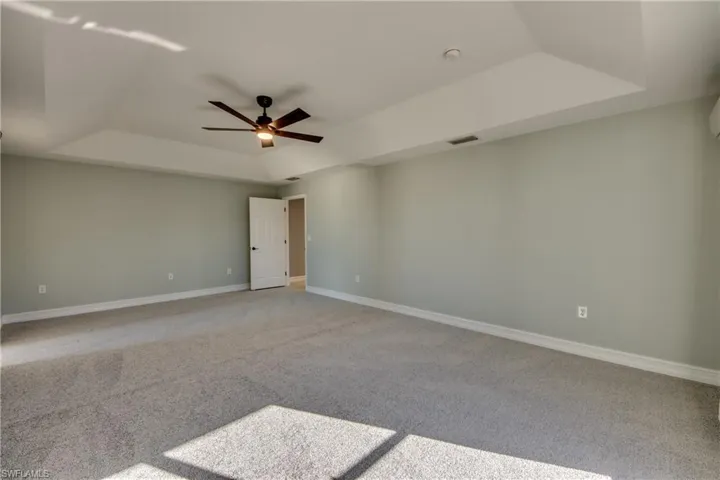 Carpeted primary bedroom featuring ceiling fan and a tray ceiling