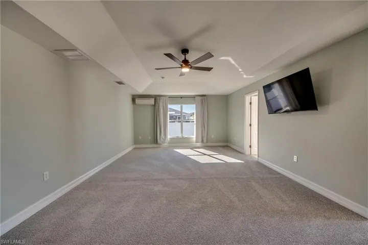Primary carpeted bedroom with an AC wall unit and ceiling fan
