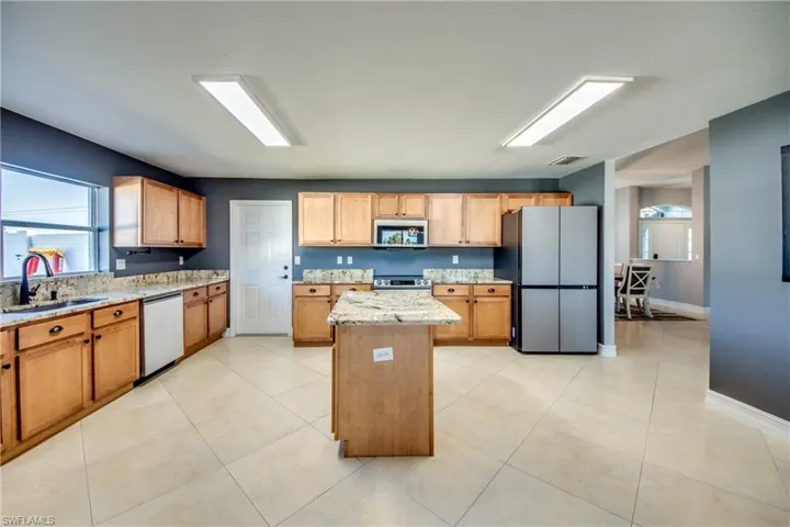 Kitchen featuring sink, a center island, light stone counters, light tile patterned floors, and appliances with stainless steel finishes