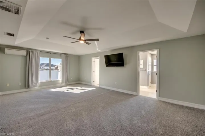 Primary carpeted bedroom with a tray ceiling, ceiling fan, and a wall mounted air conditioner