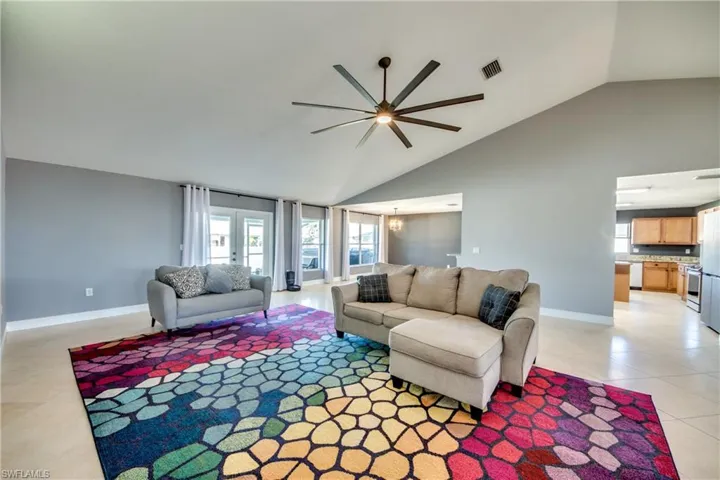 Living room featuring ceiling fan with notable chandelier, light tile patterned flooring, and vaulted ceiling