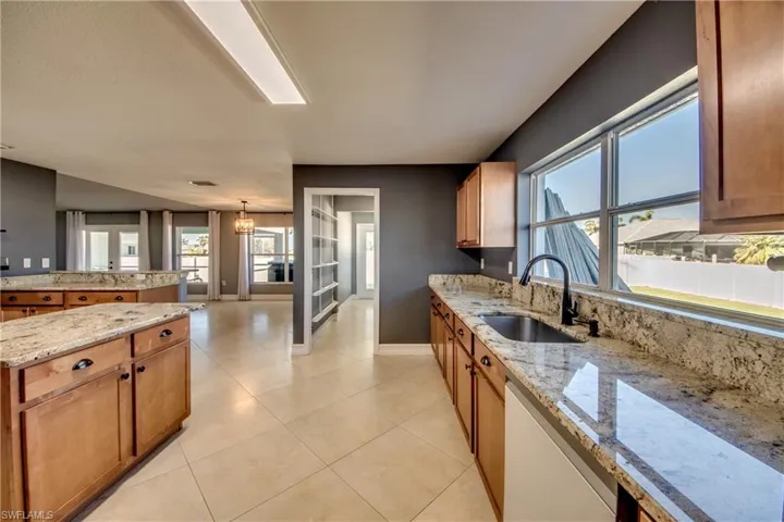 Kitchen with dishwasher, sink, hanging light fixtures, light tile patterned floors, and light stone counters