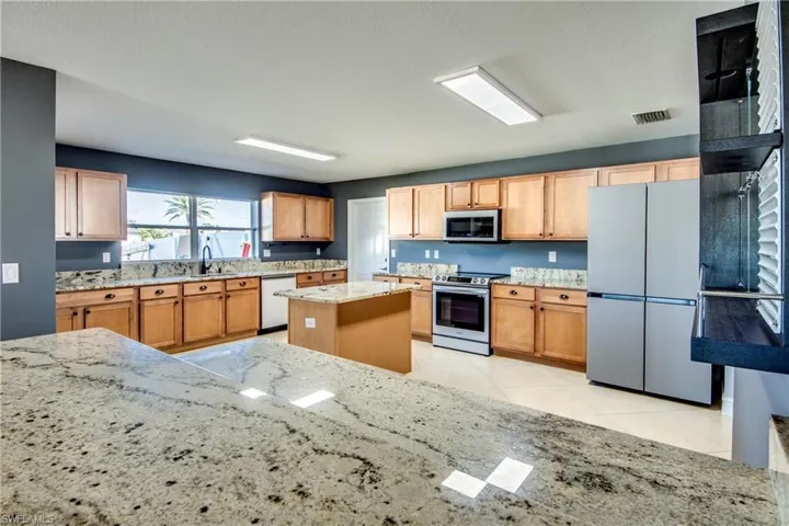 Kitchen with light stone countertops, a center island, sink, stainless steel appliances, and light tile patterned floors