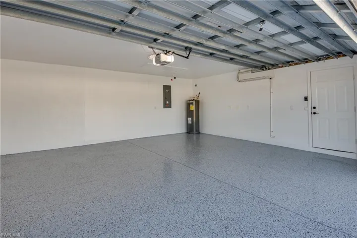 Garage with electric water heater, electric panel, a garage door opener, and a wall unit AC