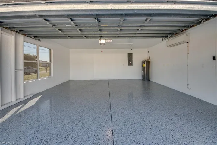 Garage with electric panel, water heater, a garage door opener, and a wall mounted air conditioner