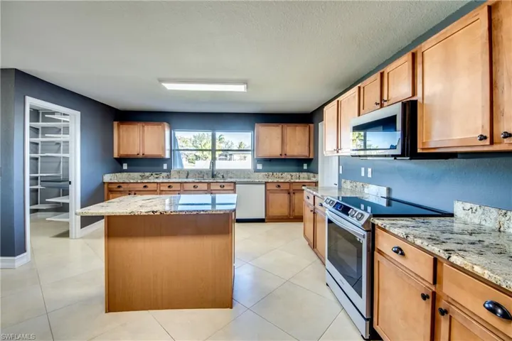 Kitchen featuring a center island, light stone counters, a textured ceiling, stainless steel electric range, and dishwashing machine