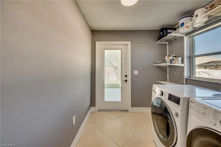 Laundry area featuring washer and dryer, light tile patterned floors, and a wealth of natural light