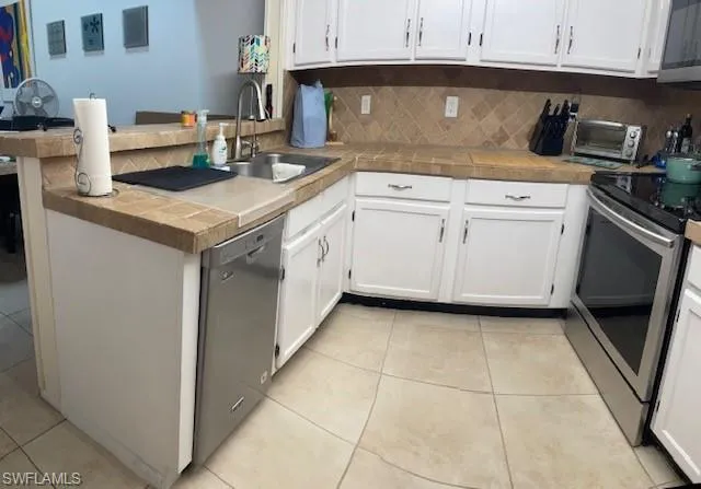 Kitchen with tile countertops, appliances with stainless steel finishes, sink, and kitchen peninsula
