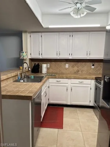 Kitchen featuring stainless steel electric stove, sink, light tile patterned flooring, white cabinets, and ceiling fan