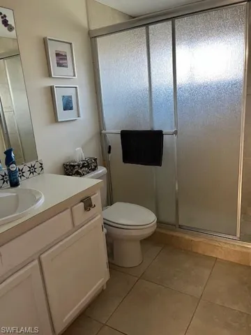Bathroom featuring a shower with door, vanity, toilet, and tile patterned floors