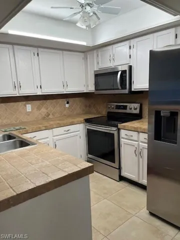 Kitchen with appliances with stainless steel finishes, tasteful backsplash, white cabinets, and ceiling fan