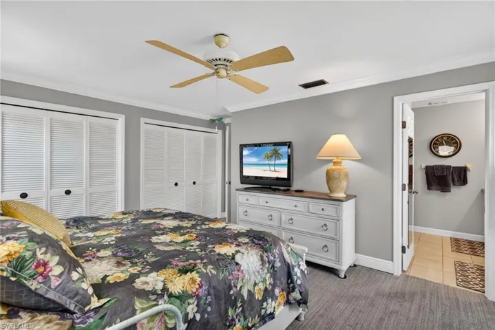 Bedroom with two closets, ornamental molding, light carpet, a ceiling fan, and light tile patterned flooring