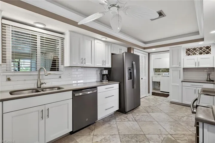 Kitchen with white cabinetry, stainless steel appliances, ceiling fan, a tray ceiling, and decorative backsplash