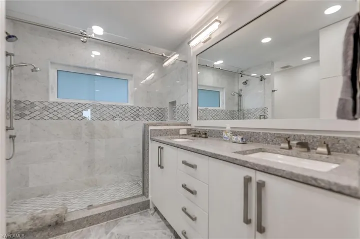 Bathroom with double vanity, a shower stall, light marble finish flooring, and recessed lighting