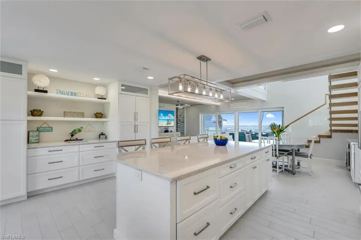 Kitchen featuring white cabinets, open shelves, a breakfast bar, pendant lighting, and light stone counters