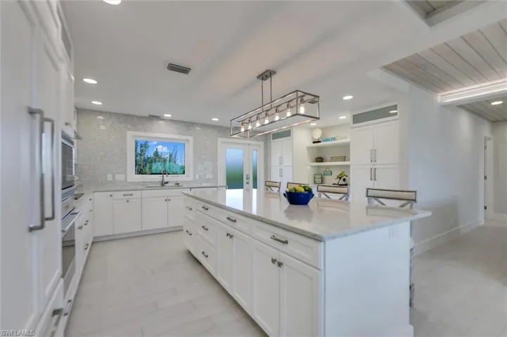 Kitchen with white cabinets, a breakfast bar, light stone counters, a kitchen island, and decorative light fixtures