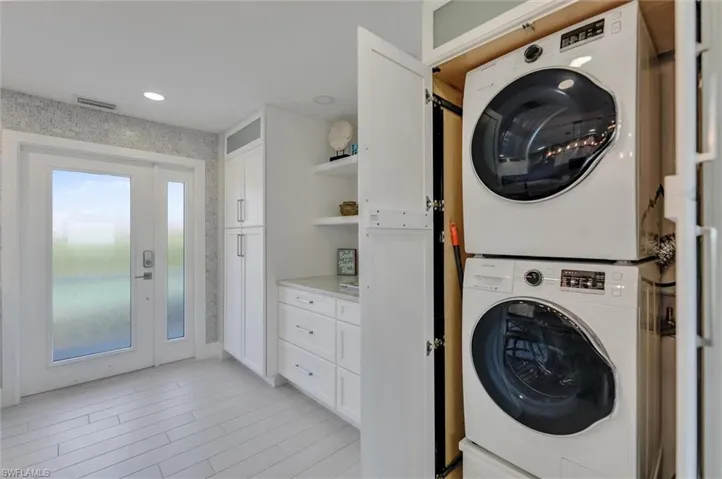 Laundry area featuring stacked washer / drying machine, wallpapered walls, and light wood-type flooring