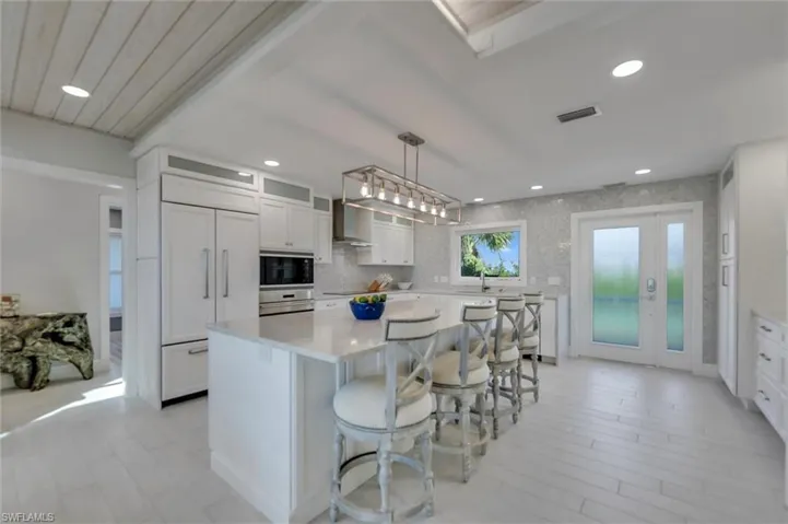 Kitchen featuring a kitchen breakfast bar, hanging light fixtures, white cabinets, a center island, and built in appliances
