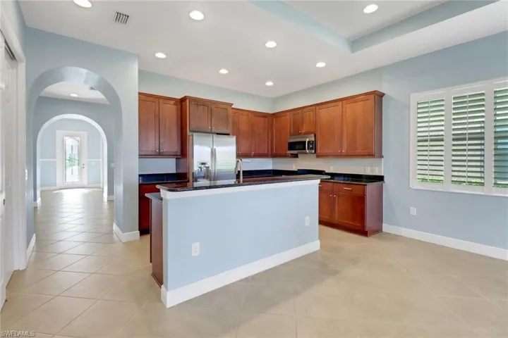 Kitchen with arched walkways, stainless steel appliances, recessed lighting, light tile patterned flooring, and an island with sink