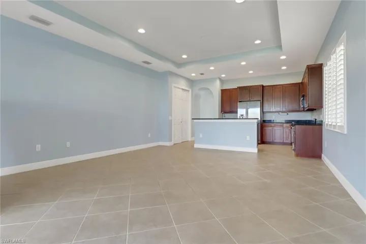 Unfurnished living room featuring recessed lighting, a raised ceiling, arched walkways, and light tile floors