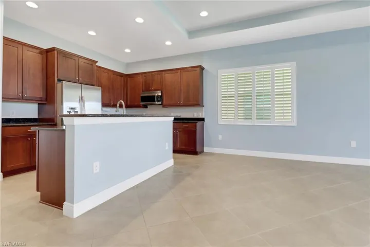 Kitchen with refrigerator with ice dispenser, a center island with sink, stainless steel microwave, recessed lighting, and light tile flooring