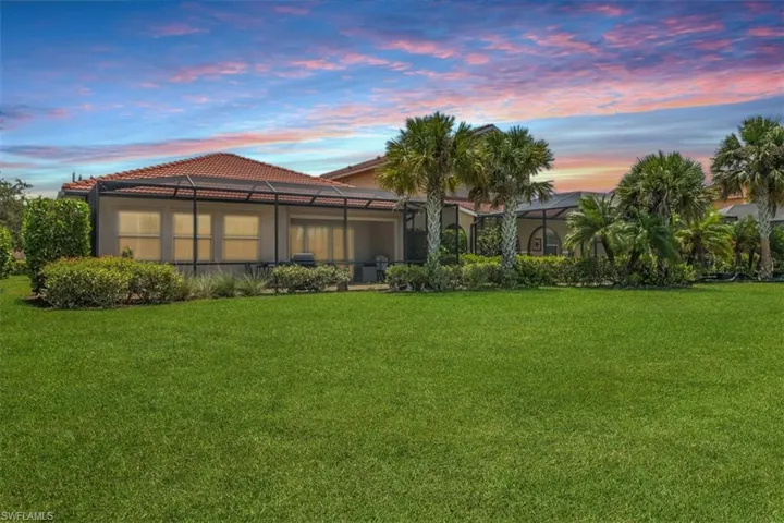 Twilight Back of property with a lawn, a tile roof, stucco siding, and screen enclosure