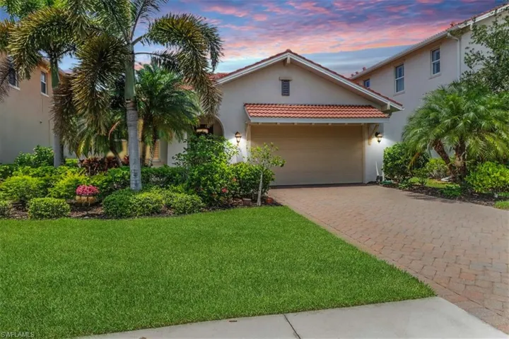 Twilight view of Mediterranean home with stucco siding, an attached garage, driveway, a yard, and a tiled roof