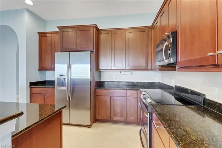 Kitchen with stainless steel appliances, dark granite counters, light tile patterned flooring, recessed lighting, and arched walkways