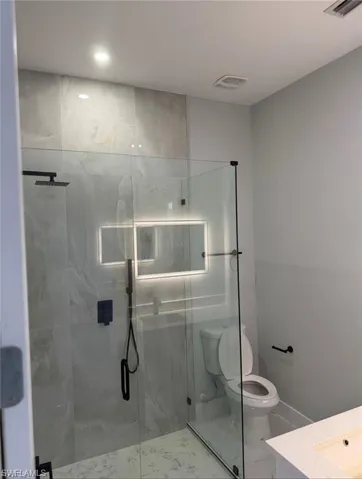 Modern bathroom featuring a glass-enclosed shower with matte black fixtures, an illuminated mirror, and large format wall tiling
