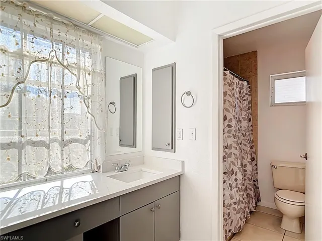 Bathroom featuring healthy amount of natural light, vanity, curtained shower, and light tile patterned floors