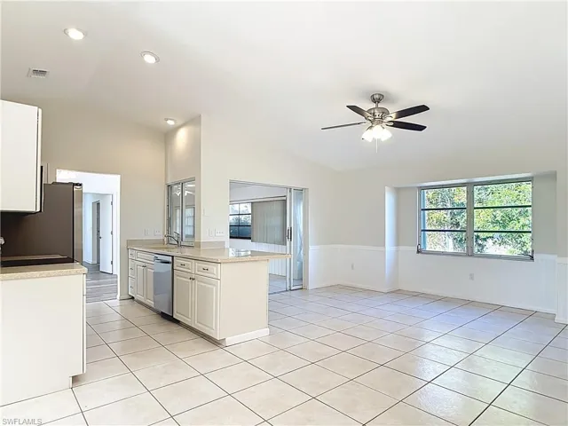 Kitchen with white cabinets, vaulted ceiling, stainless steel appliances, light stone counters, and a ceiling fan