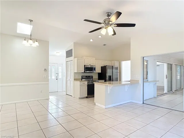 Kitchen featuring a kitchen bar, stainless steel appliances, a chandelier, light tile patterned floors, and a peninsula