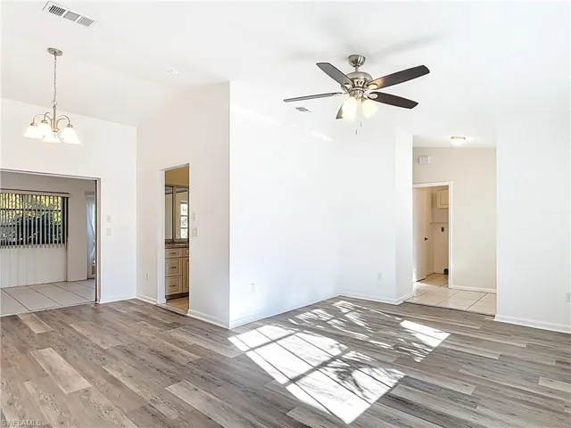 Empty room with vaulted ceiling, light wood-style flooring, a chandelier, and a ceiling fan