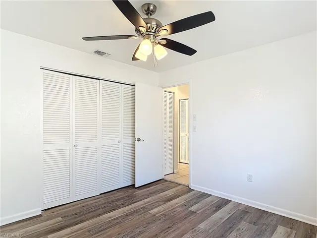 Unfurnished bedroom with a closet, dark wood-type flooring, and a ceiling fan