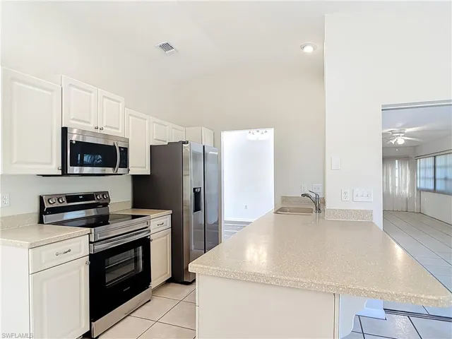 Kitchen featuring stainless steel appliances, a breakfast bar area, a peninsula, light tile patterned floors, and white cabinets