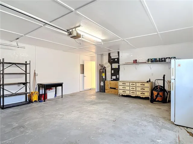 Garage featuring freestanding refrigerator, electric water heater, a garage door opener, and heating unit
