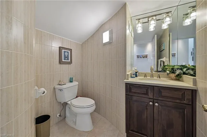 Bathroom featuring toilet, tile walls, tile patterned flooring, lofted ceiling, and vanity