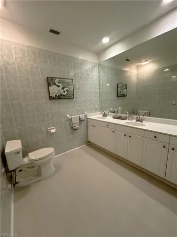 Full bathroom with tile walls, toilet, double vanity, and a sink