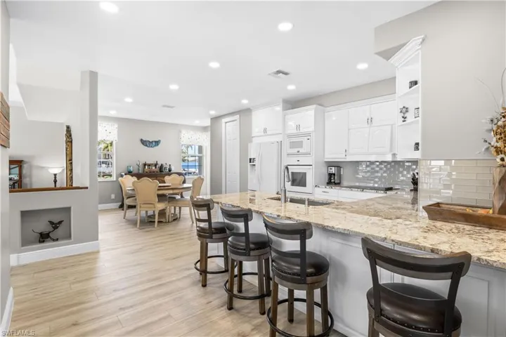 Kitchen featuring light stone counters, a peninsula, white cabinets, white appliances, and a sink