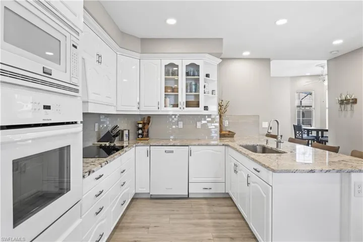 Kitchen with tasteful backsplash, a peninsula, white cabinets, white appliances, and a sink