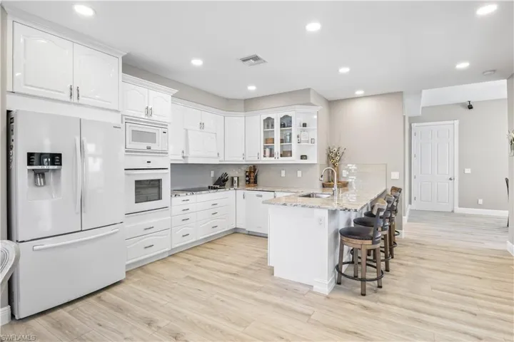 Kitchen featuring white appliances, visible vents, a peninsula, a sink, and white cabinets