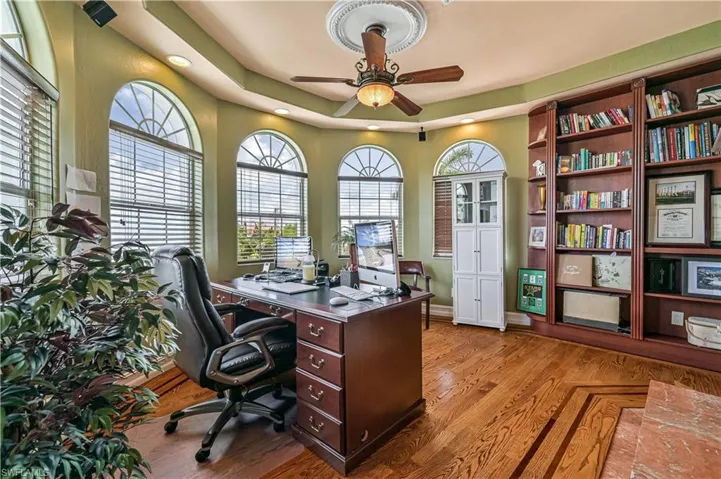 Home office with a raised ceiling, a ceiling fan, and wood finished floors