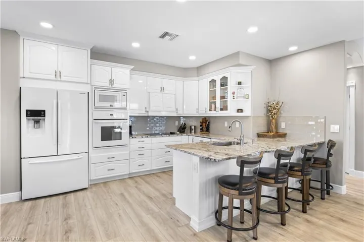 Kitchen featuring visible vents, a sink, white appliances, a peninsula, and white cabinets