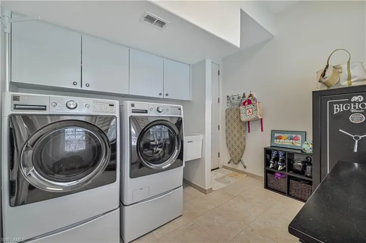Clothes washing area with visible vents, baseboards, washer and clothes dryer, light tile patterned floors, and cabinet space