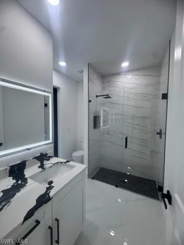 Full bath with vanity, a marble finish shower, marble finish flooring, and recessed lighting