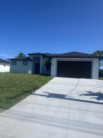 View of front facade with a garage, driveway, a front yard, and stucco siding