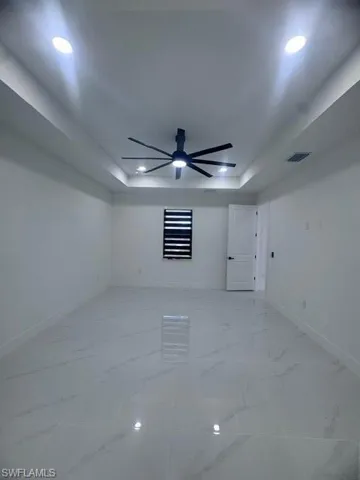 Unfurnished room with a tray ceiling, a ceiling fan, light marble finish floors, and recessed lighting